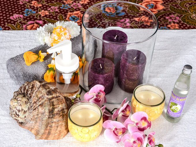 Kerzen, Massageöl, Orchideen und eine Muschel auf einem weißen Tuch.