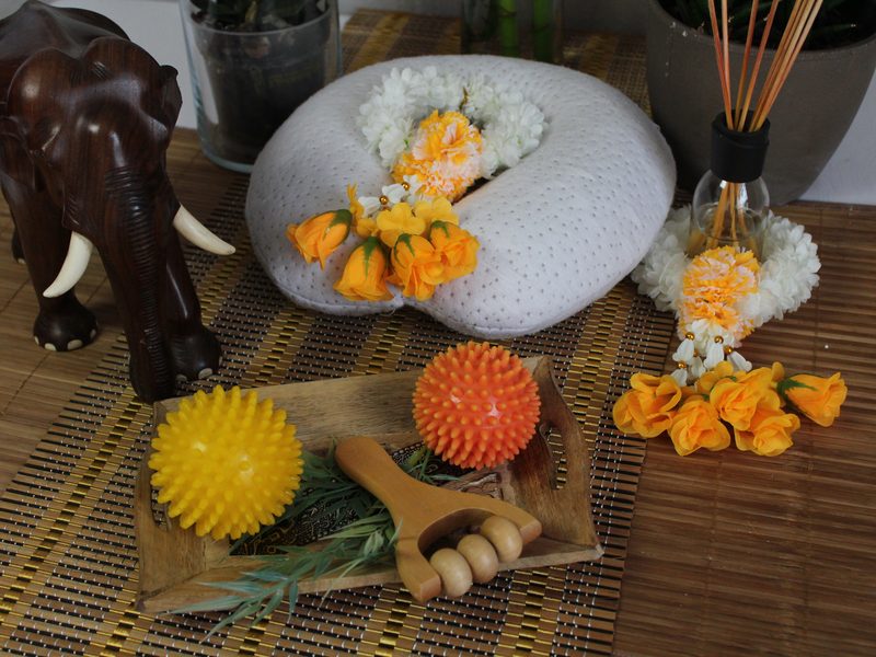 Holzelefant, Ringelblumen, Massagebälle und Räucherstäbchen auf einer Bastmatte.