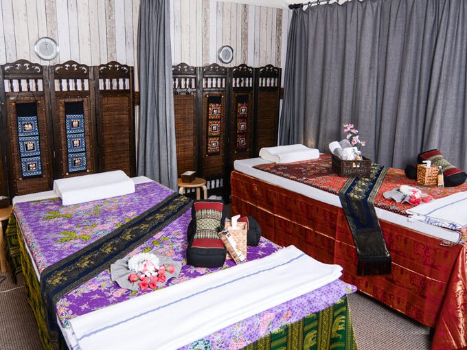 Zwei hergerichtete Massagebetten mit Kissen, Handtüchern und thailändischer Dekoration.