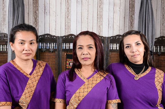 Drei Masseurinnen in traditioneller violetter Kleidung nebeneinander im Studio.