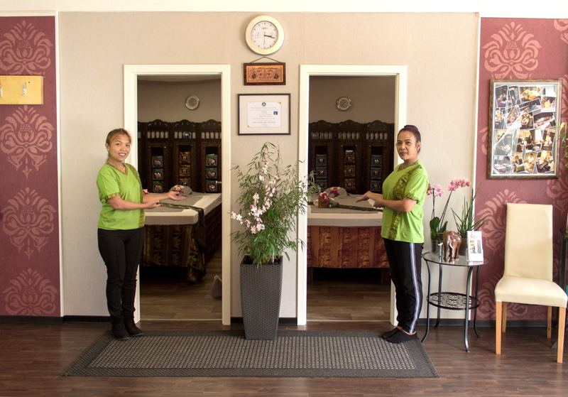 Zwei Mitarbeiterinnen von Keona's Thai Massage in grünen Shirts begrüßen im Empfangsbereich des Studios vor den Massageräumen.